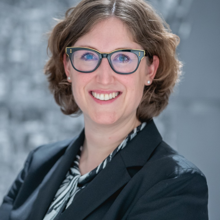 Headshot vor grauem Hintergrund. Lächelnd.